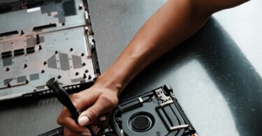 Mano con destornillador reparando el interior de un portátil: placa base y ventilador