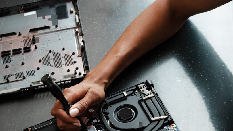 Mano con destornillador reparando el interior de un portátil: placa base y ventilador